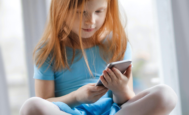  Little girl sitting on floor looks at a cell phone.