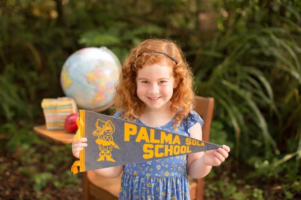 smiling girl holds "Palma Sola School" flag