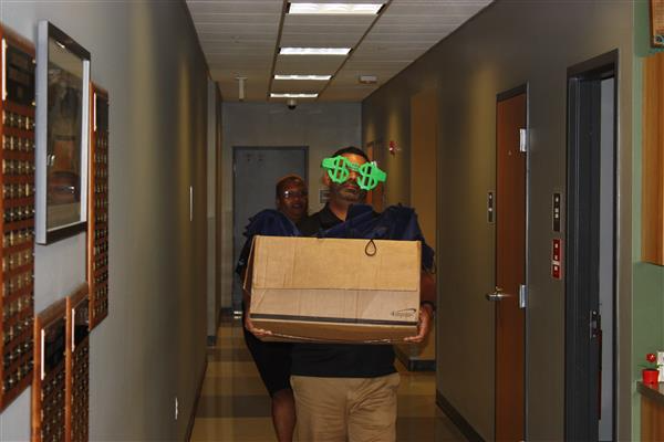 employee wearing giant silly sunglasses carries big cardboard box
